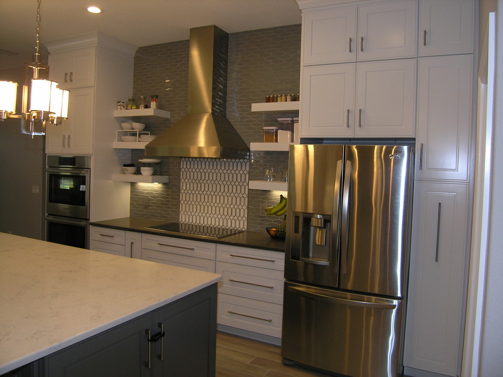 This is an example of a large contemporary galley kitchen/diner in Tampa with a submerged sink, raised-panel cabinets, white cabinets, engineered stone countertops, grey splashback, glass tiled splashback, stainless steel appliances, porcelain flooring, an island, grey floors and grey worktops.