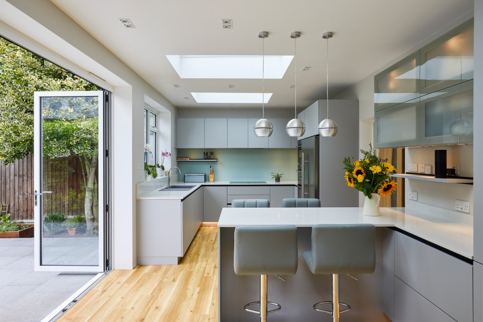 Exempel på ett mellanstort modernt vit vitt kök, med släta luckor, grå skåp, bänkskiva i kvartsit, grönt stänkskydd, glaspanel som stänkskydd, rostfria vitvaror och en halv köksö