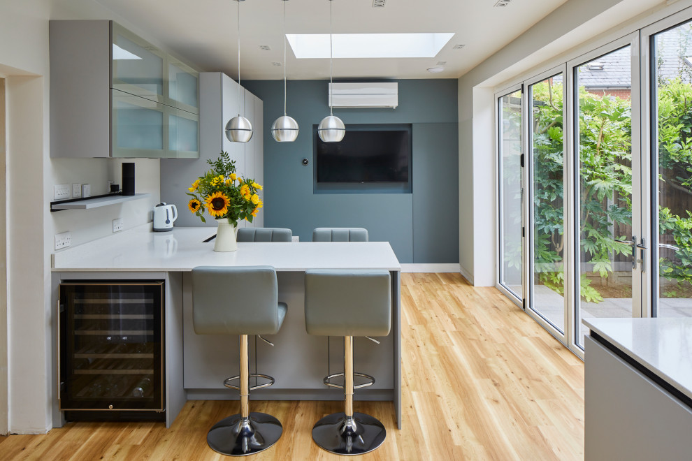 Foto på ett mellanstort funkis vit kök, med släta luckor, grå skåp, bänkskiva i kvartsit, grönt stänkskydd, glaspanel som stänkskydd, rostfria vitvaror och en halv köksö