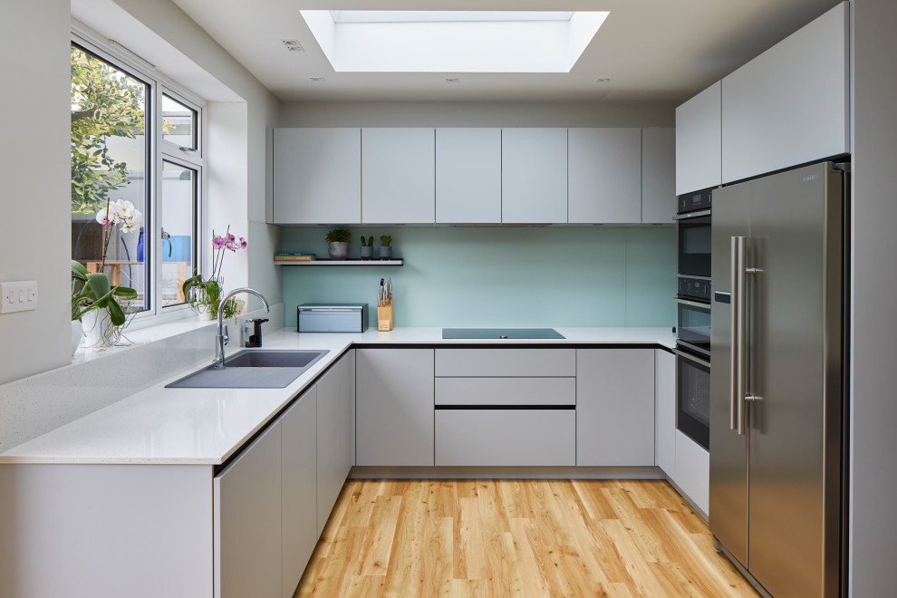 Mid-sized trendy u-shaped eat-in kitchen photo in London with flat-panel cabinets, gray cabinets, quartzite countertops, green backsplash, glass sheet backsplash, stainless steel appliances, a peninsula and white countertops