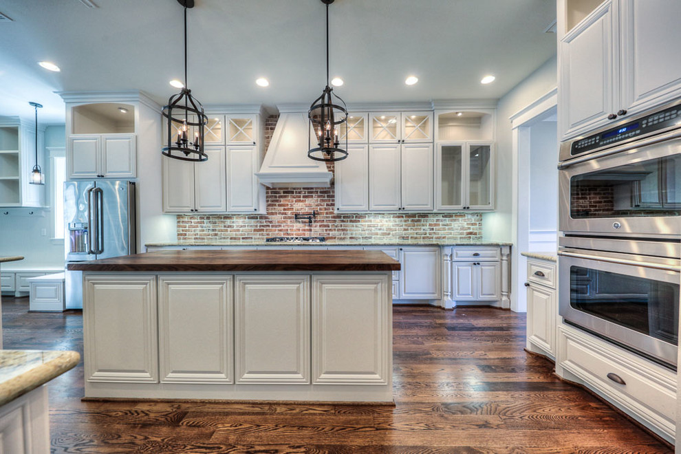 Inspiration for a large craftsman galley dark wood floor open concept kitchen remodel in Houston with a farmhouse sink, raised-panel cabinets, white cabinets, wood countertops, red backsplash, stone tile backsplash, stainless steel appliances and an island