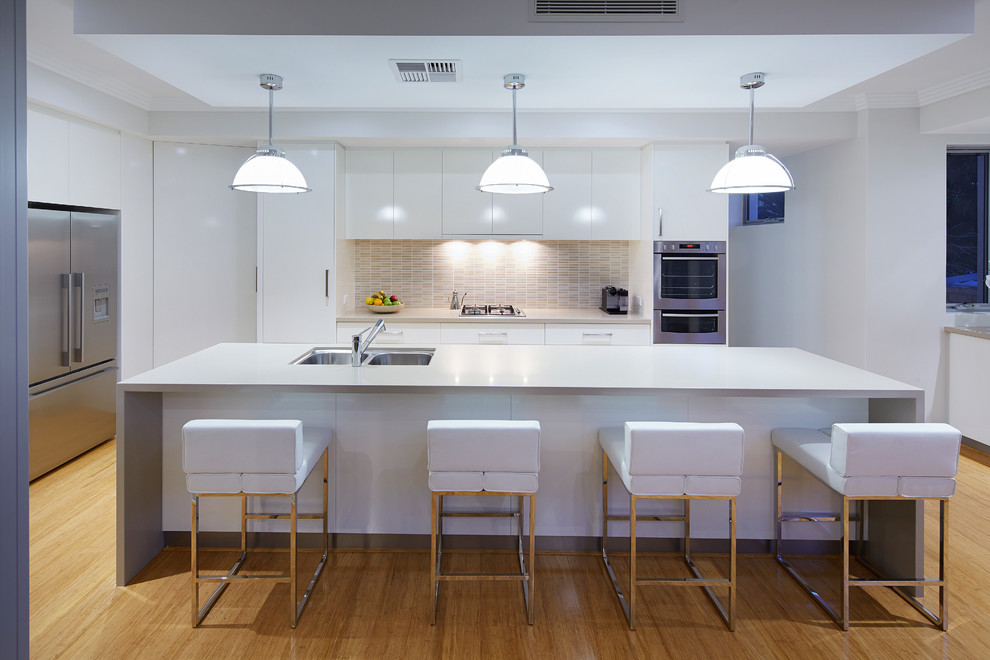 Foto på ett funkis u-kök, med en dubbel diskho, släta luckor, vita skåp, beige stänkskydd, stänkskydd i mosaik, rostfria vitvaror, mellanmörkt trägolv och en köksö