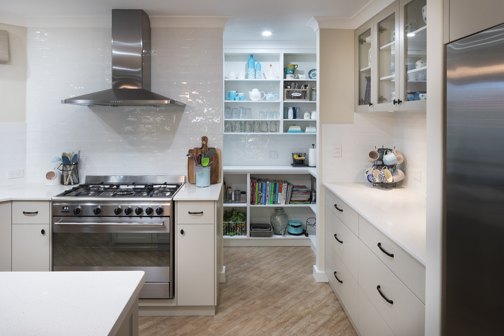 This is an example of a traditional kitchen in Perth with flat-panel cabinets, beige cabinets, engineered stone countertops, white splashback, metro tiled splashback, stainless steel appliances, an island and white worktops.