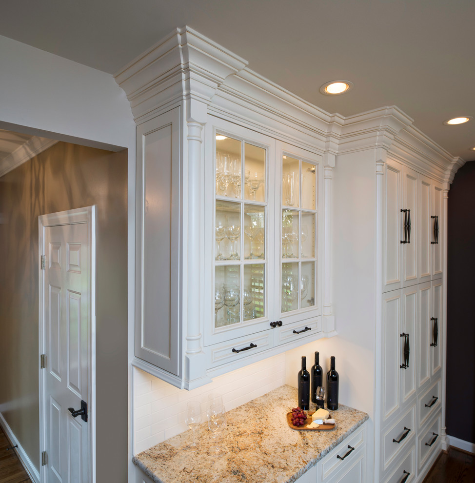 Exempel på ett mellanstort klassiskt kök, med en undermonterad diskho, luckor med infälld panel, vita skåp, granitbänkskiva, vitt stänkskydd, stänkskydd i tunnelbanekakel, rostfria vitvaror, mörkt trägolv, en köksö och brunt golv