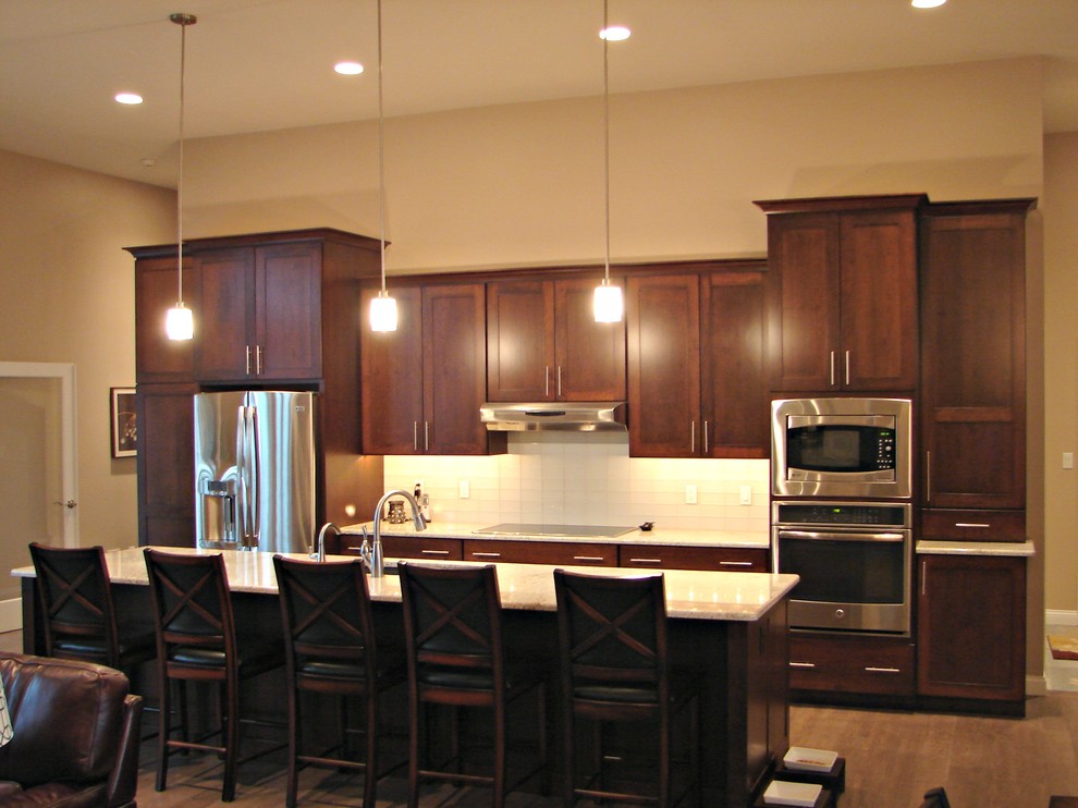 Exempel på ett mellanstort modernt linjärt kök och matrum, med en undermonterad diskho, skåp i shakerstil, skåp i mörkt trä, granitbänkskiva, vitt stänkskydd, stänkskydd i keramik, rostfria vitvaror, mörkt trägolv och en köksö