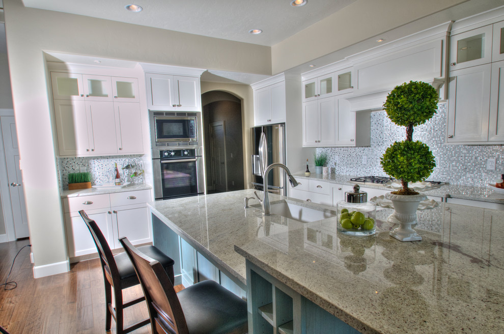 Exempel på ett stort klassiskt flerfärgad flerfärgat kök, med en undermonterad diskho, släta luckor, vita skåp, granitbänkskiva, blått stänkskydd, stänkskydd i mosaik, rostfria vitvaror, mörkt trägolv, en köksö och brunt golv