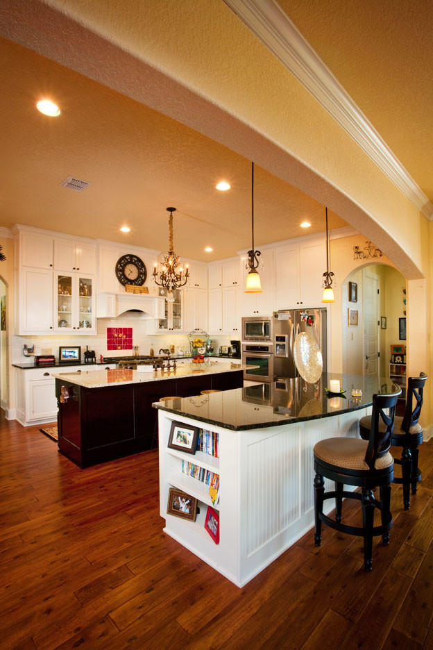 Offene, Zweizeilige Klassische Küche mit weißen Schränken, Granit-Arbeitsplatte, braunem Holzboden und zwei Kücheninseln in Austin