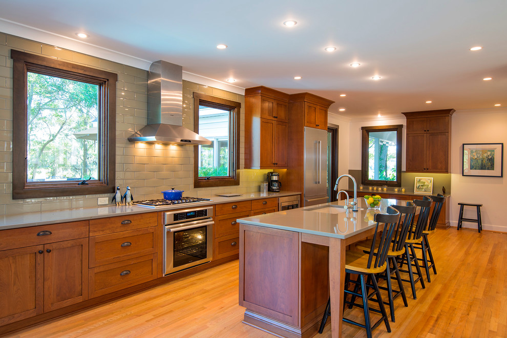 Photo of a large traditional single-wall open plan kitchen in Charleston with a submerged sink, shaker cabinets, medium wood cabinets, engineered stone countertops, beige splashback, glass tiled splashback, stainless steel appliances, light hardwood flooring and an island.