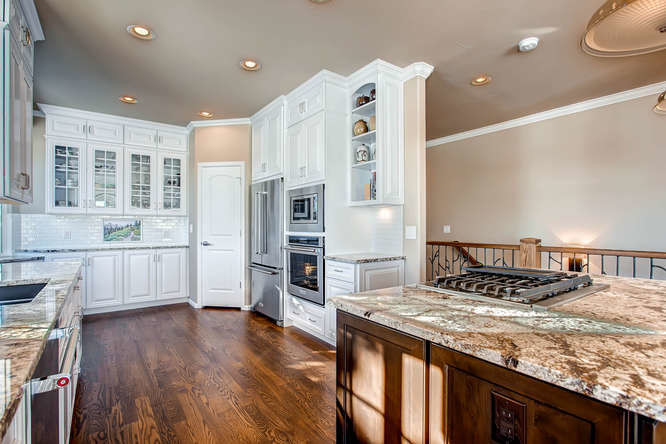 Foto på ett mellanstort vintage kök, med en undermonterad diskho, luckor med upphöjd panel, vita skåp, granitbänkskiva, vitt stänkskydd, stänkskydd i porslinskakel, rostfria vitvaror, mellanmörkt trägolv, en köksö och brunt golv