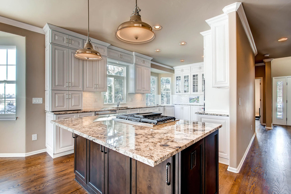 Example of a mid-sized transitional u-shaped medium tone wood floor and brown floor open concept kitchen design in Denver with an undermount sink, raised-panel cabinets, white cabinets, granite countertops, white backsplash, porcelain backsplash, stainless steel appliances, an island and brown countertops