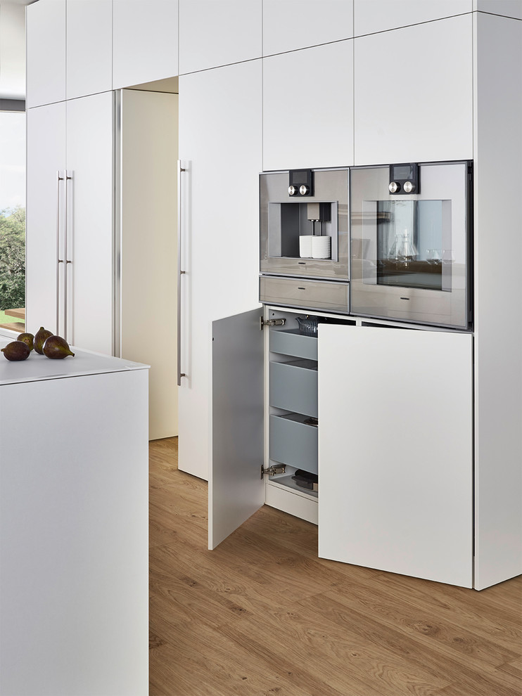 Modelo de cocina minimalista grande con armarios con paneles lisos, puertas de armario blancas, encimera de cuarzo compacto, suelo de madera clara y una isla