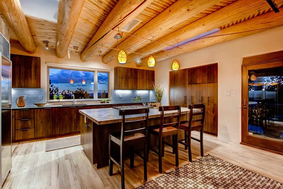 Große Mediterrane Wohnküche in L-Form mit flächenbündigen Schrankfronten, Küchengeräten aus Edelstahl, Kücheninsel, Unterbauwaschbecken, dunklen Holzschränken, Granit-Arbeitsplatte, Küchenrückwand in Grau, Rückwand aus Metrofliesen und braunem Holzboden in Albuquerque