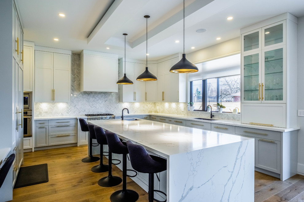Moderne Küche in L-Form mit Unterbauwaschbecken, Glasfronten, weißen Schränken, Küchenrückwand in Grau, Küchengeräten aus Edelstahl, braunem Holzboden, Kücheninsel und weißer Arbeitsplatte in Toronto