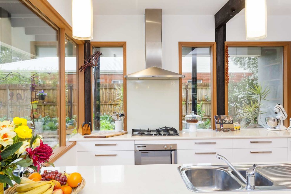 This is an example of a medium sized midcentury u-shaped kitchen/diner in Melbourne with a double-bowl sink, flat-panel cabinets, white cabinets, white splashback, glass sheet splashback, stainless steel appliances, medium hardwood flooring, an island and white worktops.