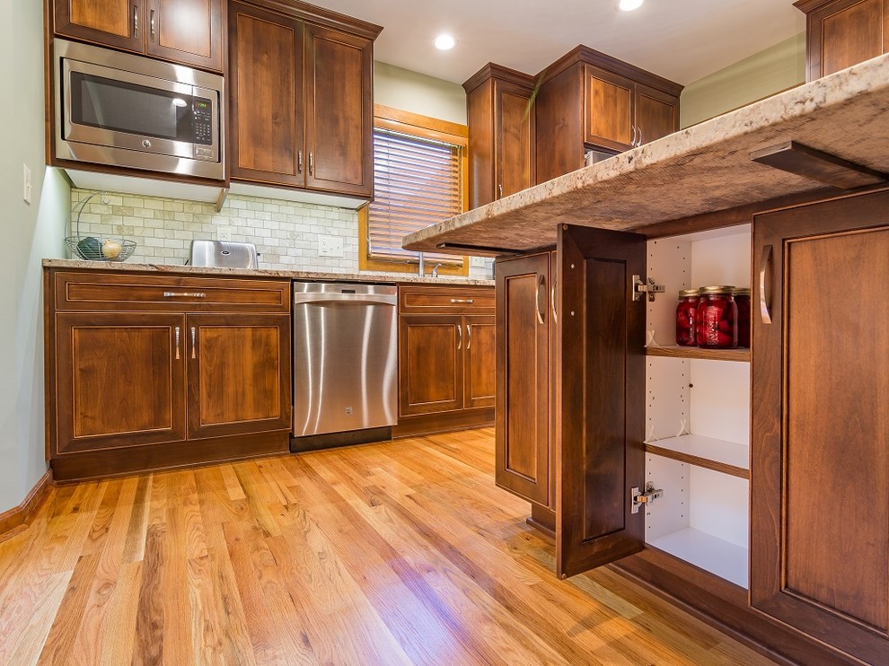 Exempel på ett avskilt, mellanstort klassiskt l-kök, med en undermonterad diskho, släta luckor, bruna skåp, granitbänkskiva, beige stänkskydd, stänkskydd i stenkakel, rostfria vitvaror, ljust trägolv och en köksö