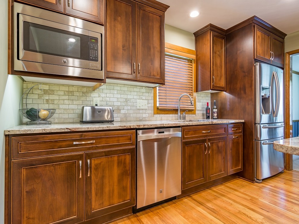 Example of a mid-sized classic l-shaped light wood floor enclosed kitchen design in Kansas City with an undermount sink, flat-panel cabinets, brown cabinets, granite countertops, beige backsplash, stone tile backsplash, stainless steel appliances and an island