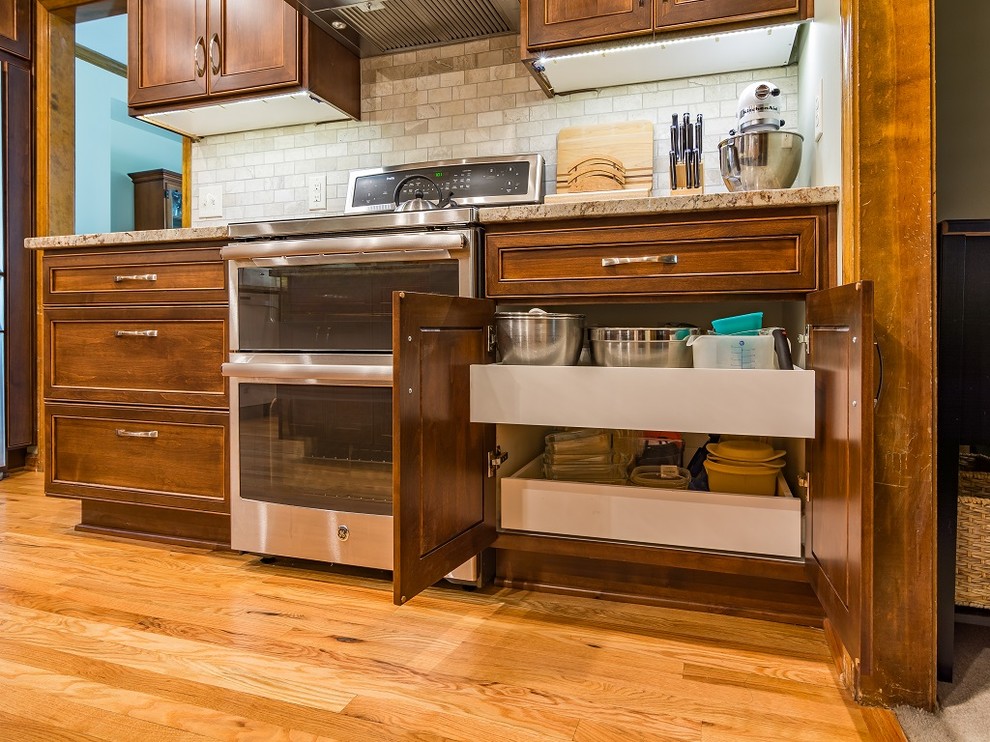 Foto på ett avskilt, mellanstort vintage l-kök, med en undermonterad diskho, släta luckor, bruna skåp, granitbänkskiva, beige stänkskydd, stänkskydd i stenkakel, rostfria vitvaror, ljust trägolv och en köksö