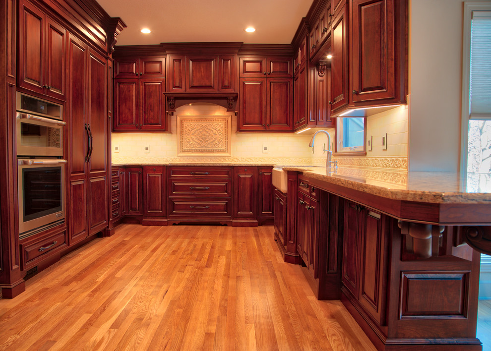 Example of a mid-sized classic galley light wood floor eat-in kitchen design in Kansas City with a farmhouse sink, raised-panel cabinets, brown cabinets, quartz countertops and paneled appliances