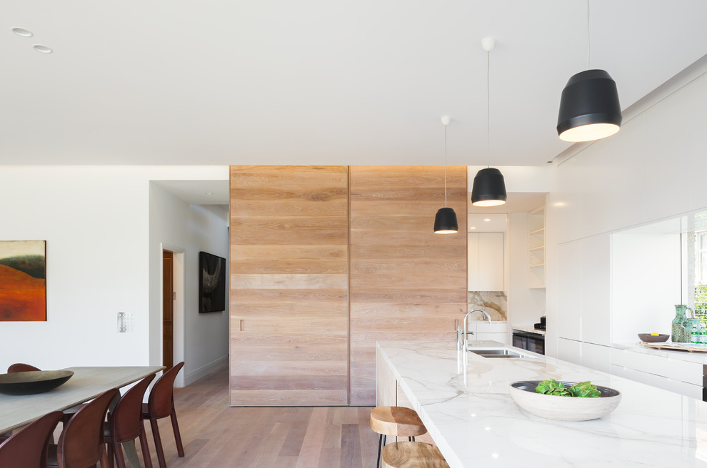 Diseño de cocina comedor lineal escandinava con fregadero bajoencimera, puertas de armario blancas, encimera de mármol, suelo de madera clara y una isla