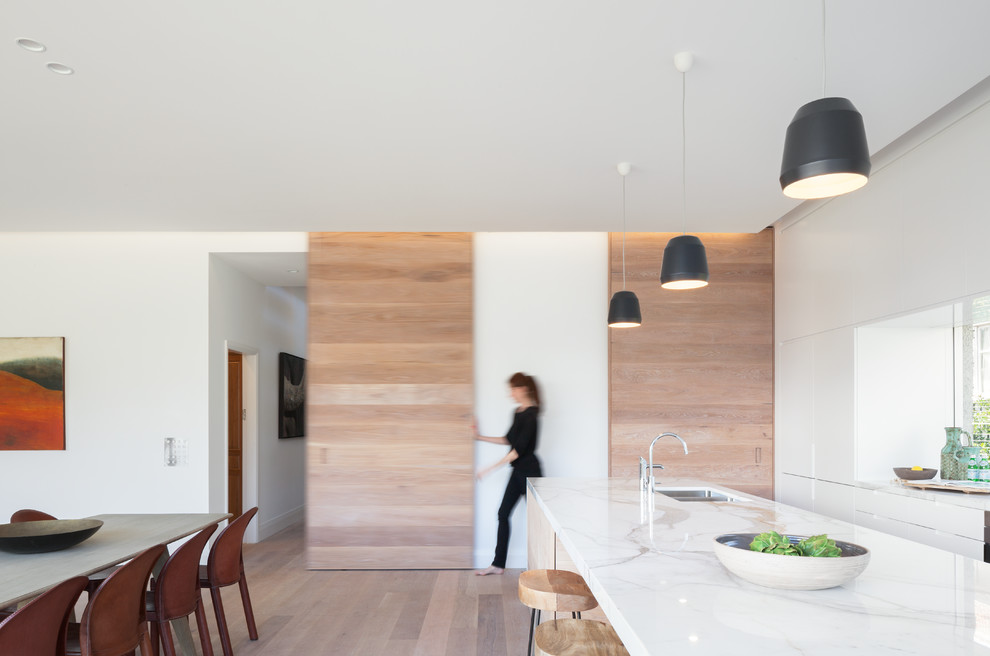 Bild på ett skandinaviskt linjärt kök och matrum, med en undermonterad diskho, vita skåp, marmorbänkskiva, ljust trägolv och en köksö