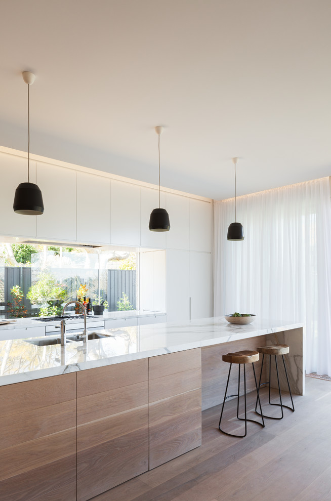 Photo of a scandinavian galley kitchen in Sydney with a submerged sink, white cabinets, marble worktops, light hardwood flooring, an island, flat-panel cabinets and glass sheet splashback.