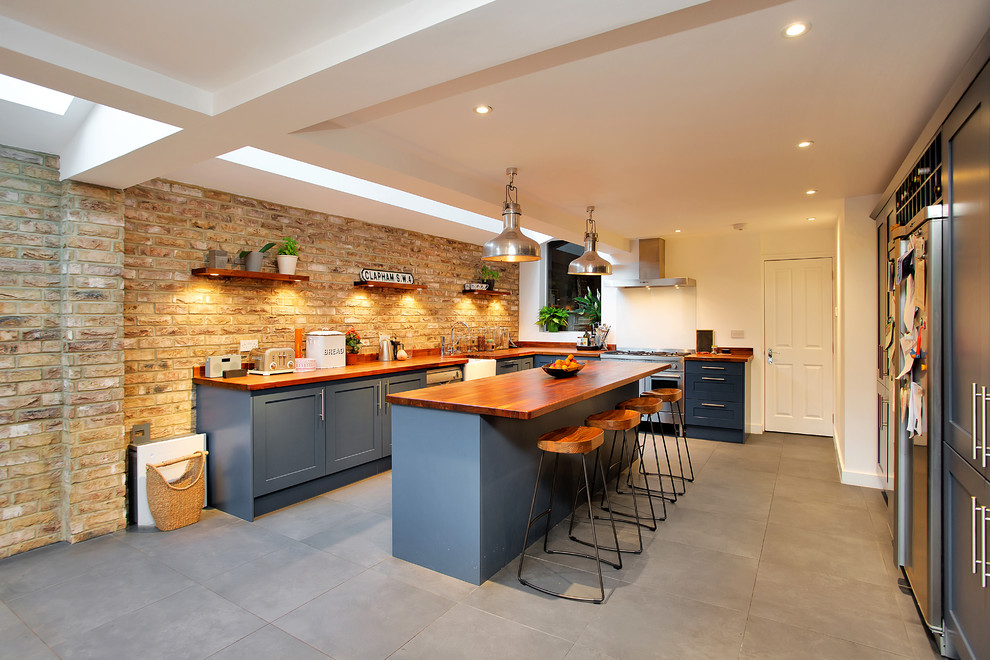 ロンドンにある広いカントリー風のおしゃれなキッチン (エプロンフロントシンク、落し込みパネル扉のキャビネット、青いキャビネット、木材カウンター、シルバーの調理設備、グレーの床、茶色いキッチンカウンター) の写真