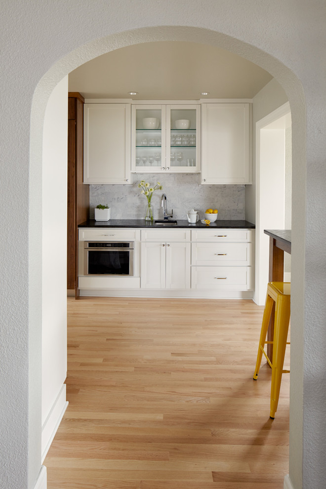 Example of a mid-sized classic galley light wood floor eat-in kitchen design in Seattle with an undermount sink, shaker cabinets, white cabinets, blue backsplash, stone tile backsplash, stainless steel appliances and no island