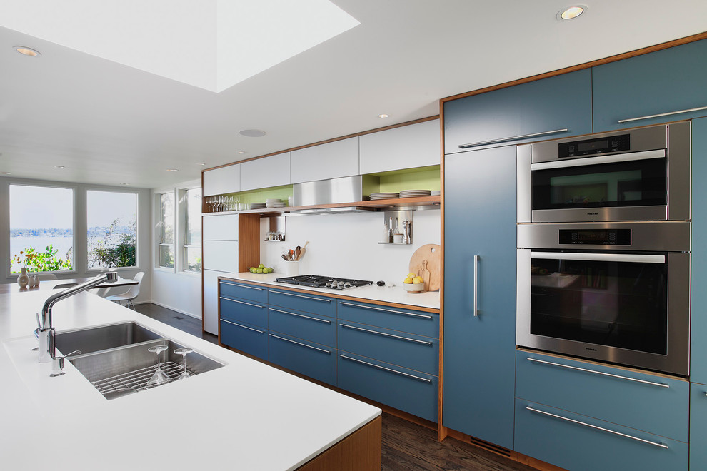 Large trendy galley dark wood floor and brown floor eat-in kitchen photo in Seattle with flat-panel cabinets, stainless steel appliances, a double-bowl sink, blue cabinets, white backsplash and an island