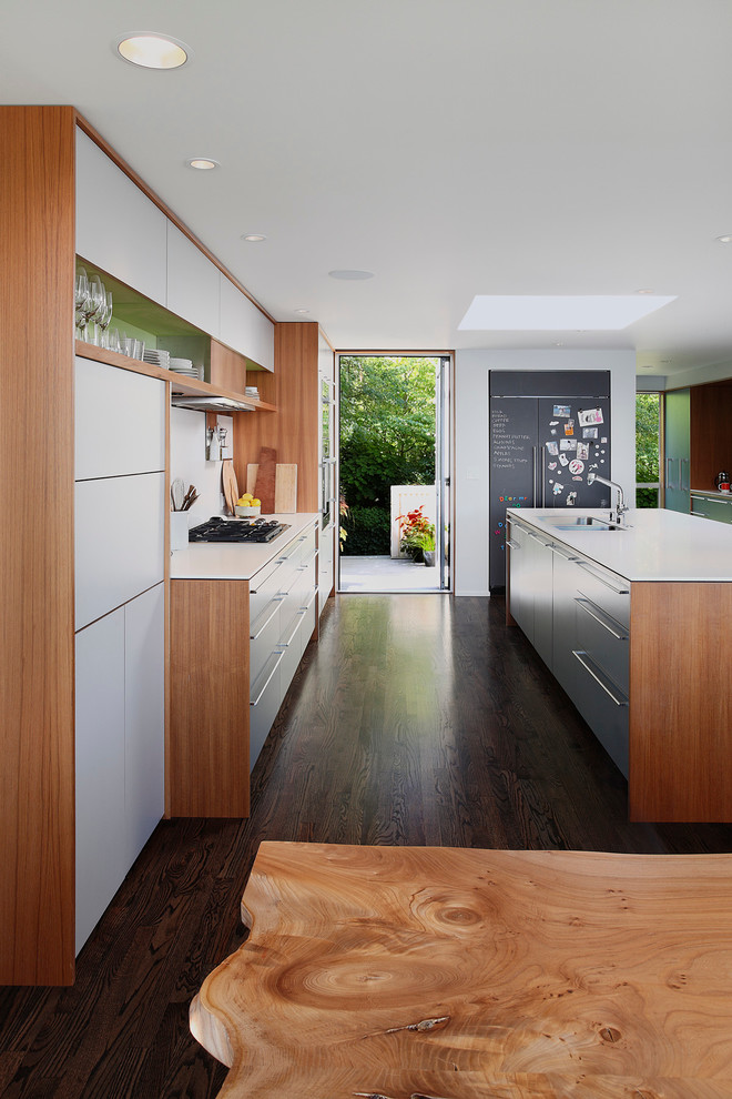Large trendy galley dark wood floor and brown floor eat-in kitchen photo in Seattle with flat-panel cabinets, an undermount sink, blue cabinets, solid surface countertops, white backsplash, paneled appliances and an island