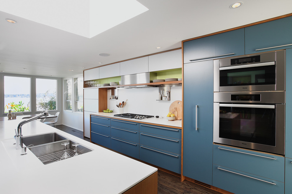 Inspiration for a medium sized midcentury galley kitchen in Seattle with a submerged sink, flat-panel cabinets, blue cabinets, stainless steel appliances, dark hardwood flooring, an island and white splashback.