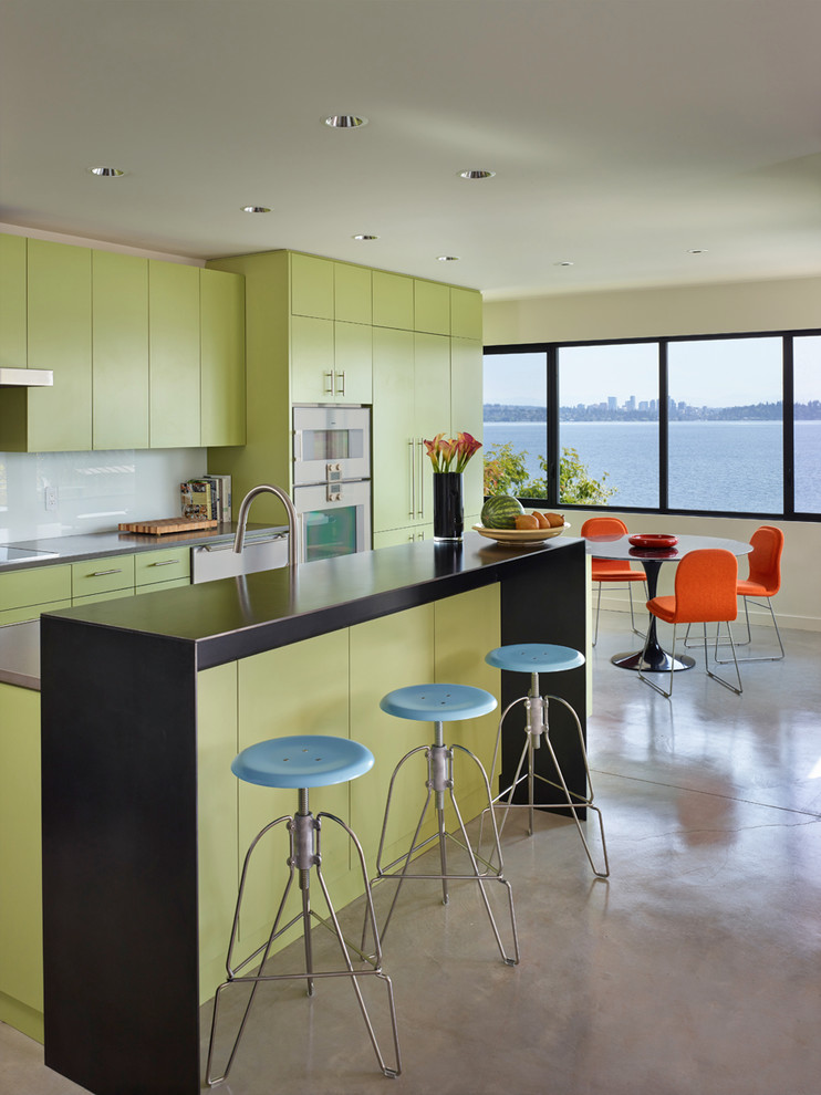 На фото: параллельная кухня в современном стиле с плоскими фасадами, обеденным столом, техникой под мебельный фасад, зелеными фасадами, белым фартуком и фартуком из стекла с