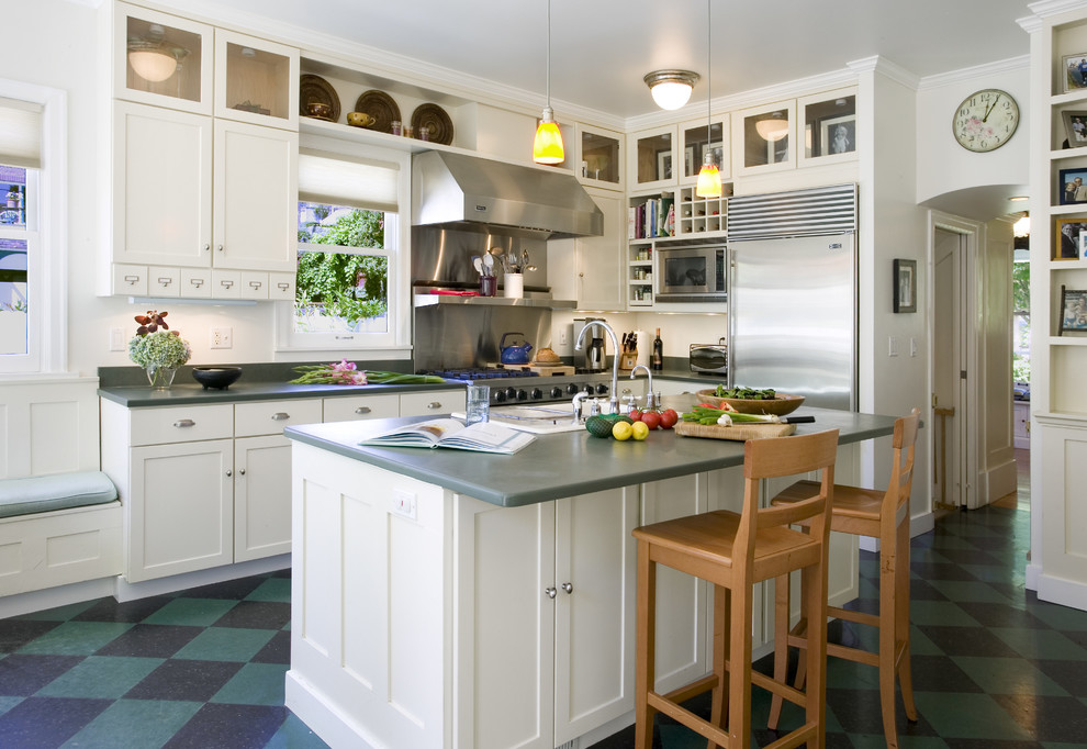 На фото: угловая кухня в классическом стиле с фасадами в стиле шейкер, белыми фасадами, техникой из нержавеющей стали и разноцветным полом с