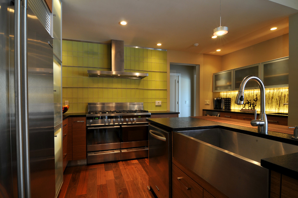 Exempel på ett modernt kök, med en rustik diskho, släta luckor, skåp i ljust trä, bänkskiva i täljsten, gult stänkskydd, stänkskydd i glaskakel och rostfria vitvaror