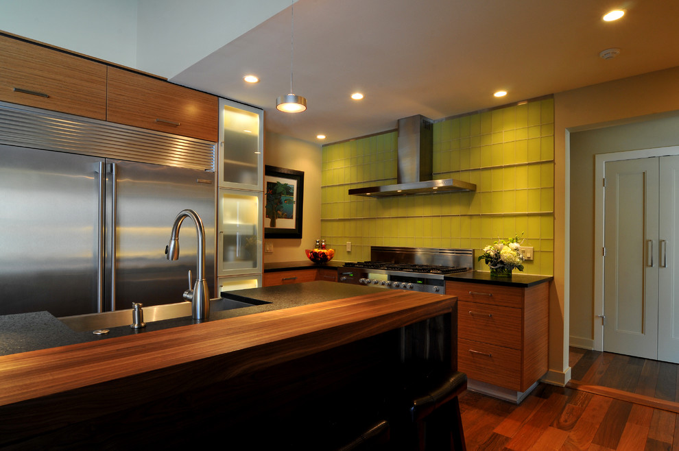 Example of a trendy u-shaped enclosed kitchen design in New York with a single-bowl sink, flat-panel cabinets, light wood cabinets, limestone countertops, yellow backsplash, glass tile backsplash and stainless steel appliances