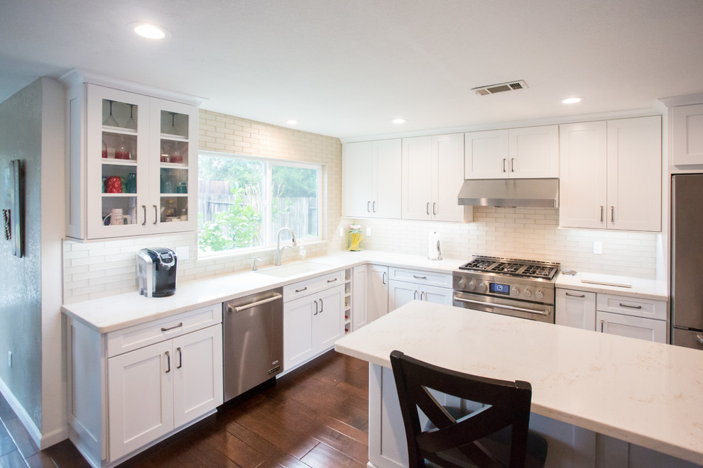 Photo of a traditional l-shaped kitchen pantry in Sacramento with a single-bowl sink, shaker cabinets, white cabinets, engineered stone countertops, beige splashback, metro tiled splashback, stainless steel appliances, medium hardwood flooring, an island and brown floors.