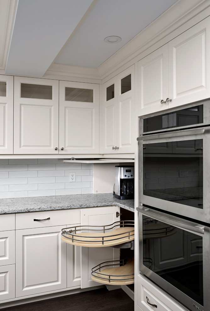 Bild på ett vintage grå grått kök, med en undermonterad diskho, luckor med upphöjd panel, vitt stänkskydd, stänkskydd i tunnelbanekakel, rostfria vitvaror, mörkt trägolv, brunt golv, granitbänkskiva och beige skåp