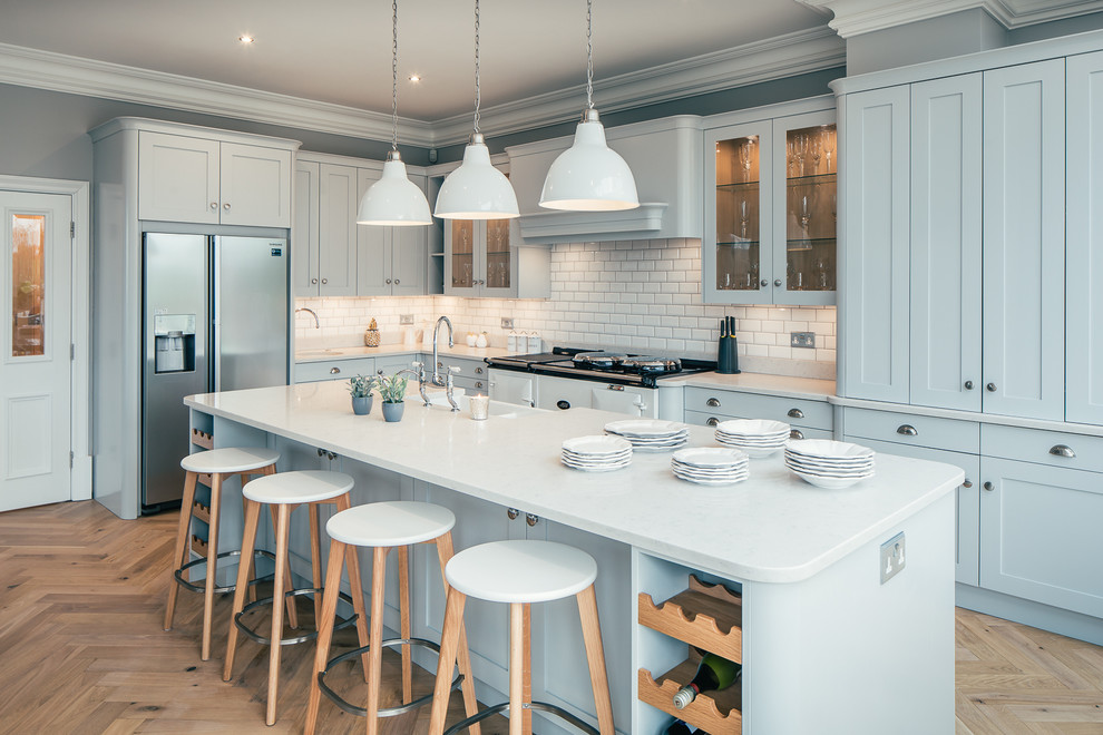 Photo of a large traditional l-shaped open plan kitchen in Hertfordshire with a built-in sink, shaker cabinets, blue cabinets, granite worktops, white splashback, ceramic splashback, stainless steel appliances, light hardwood flooring, an island and beige floors.