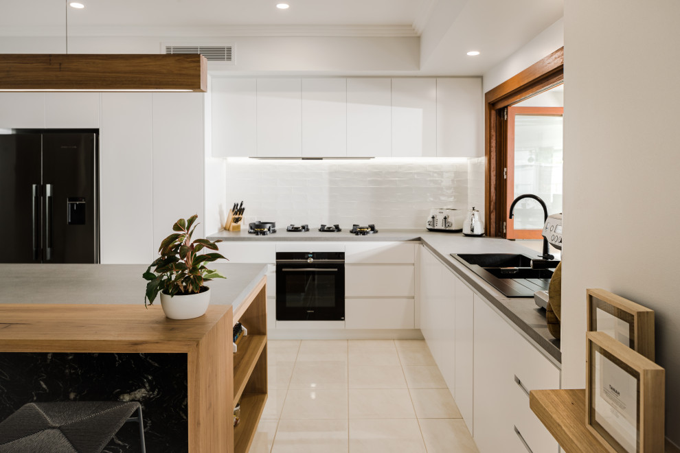 Photo of a large modern l-shaped open plan kitchen in Sunshine Coast with a double-bowl sink, granite worktops, white splashback, metro tiled splashback, white appliances, an island, beige floors, flat-panel cabinets, white cabinets, porcelain flooring, grey worktops and a drop ceiling.