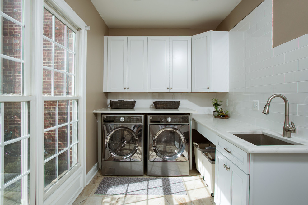 Imagen de lavadero clásico grande con puertas de armario blancas, encimera de granito, salpicadero beige y suelo de madera clara