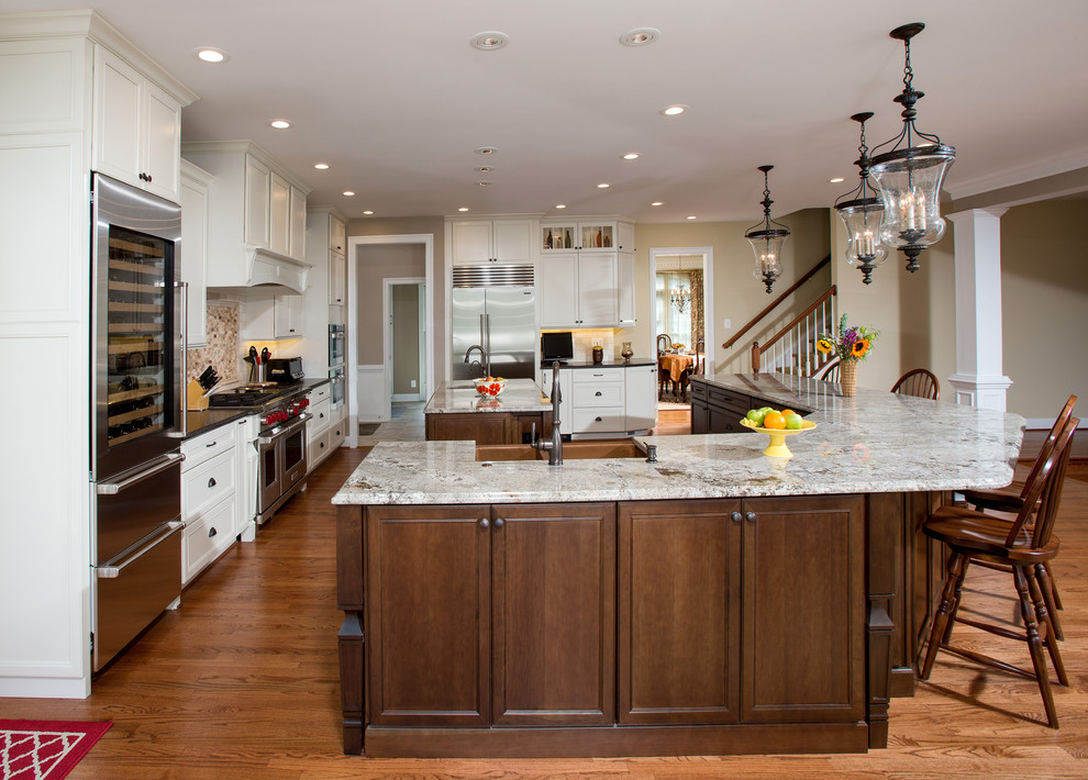 Cette photo montre une grande cuisine chic avec des portes de placard blanches, un plan de travail en granite, une crédence beige, un électroménager en acier inoxydable, parquet clair et 2 îlots.