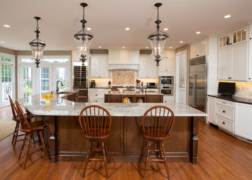 Inspiration pour une grande cuisine traditionnelle avec des portes de placard blanches, un plan de travail en granite, une crédence beige, un électroménager en acier inoxydable, 2 îlots, un évier de ferme, un placard avec porte à panneau encastré, une crédence en mosaïque et un sol en bois brun.