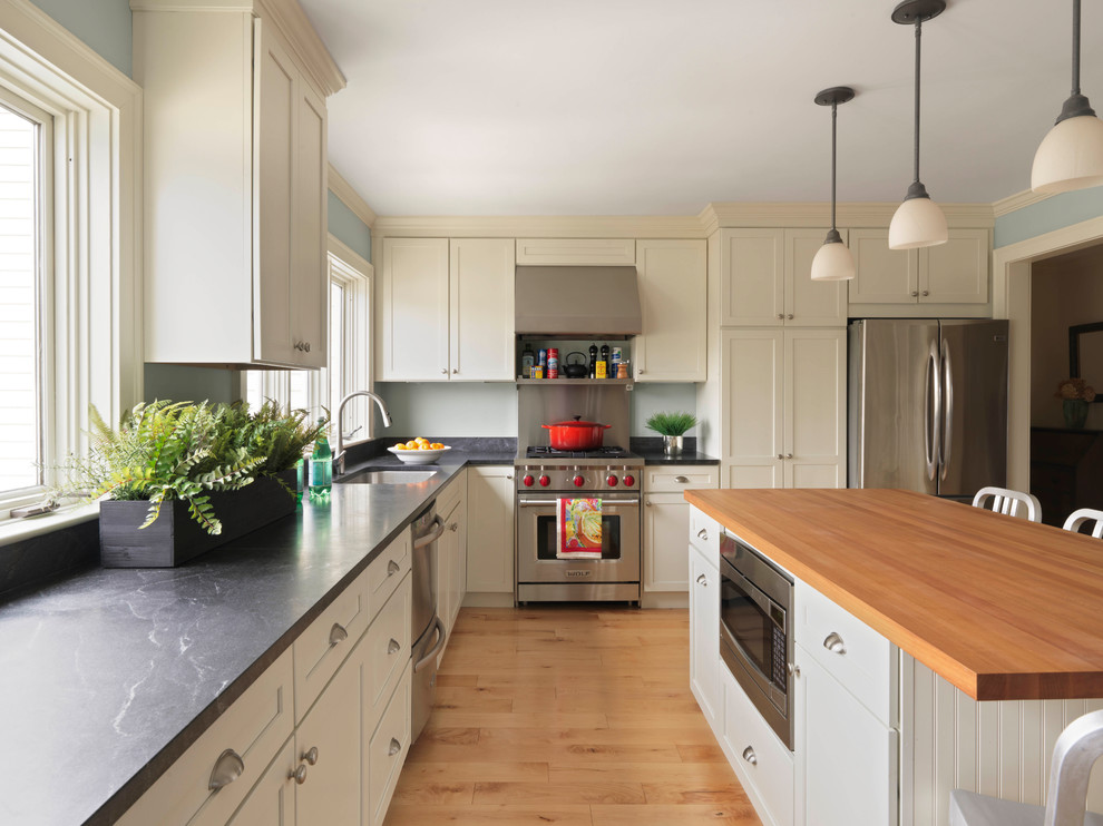 Exempel på ett klassiskt l-kök, med en undermonterad diskho, skåp i shakerstil, beige skåp, rostfria vitvaror, ljust trägolv, en köksö och brunt golv
