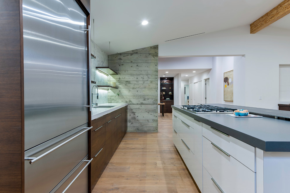 Photo of a medium sized modern galley open plan kitchen in San Diego with a built-in sink, flat-panel cabinets, medium wood cabinets, white splashback, stainless steel appliances, medium hardwood flooring, an island, composite countertops, marble splashback and brown floors.