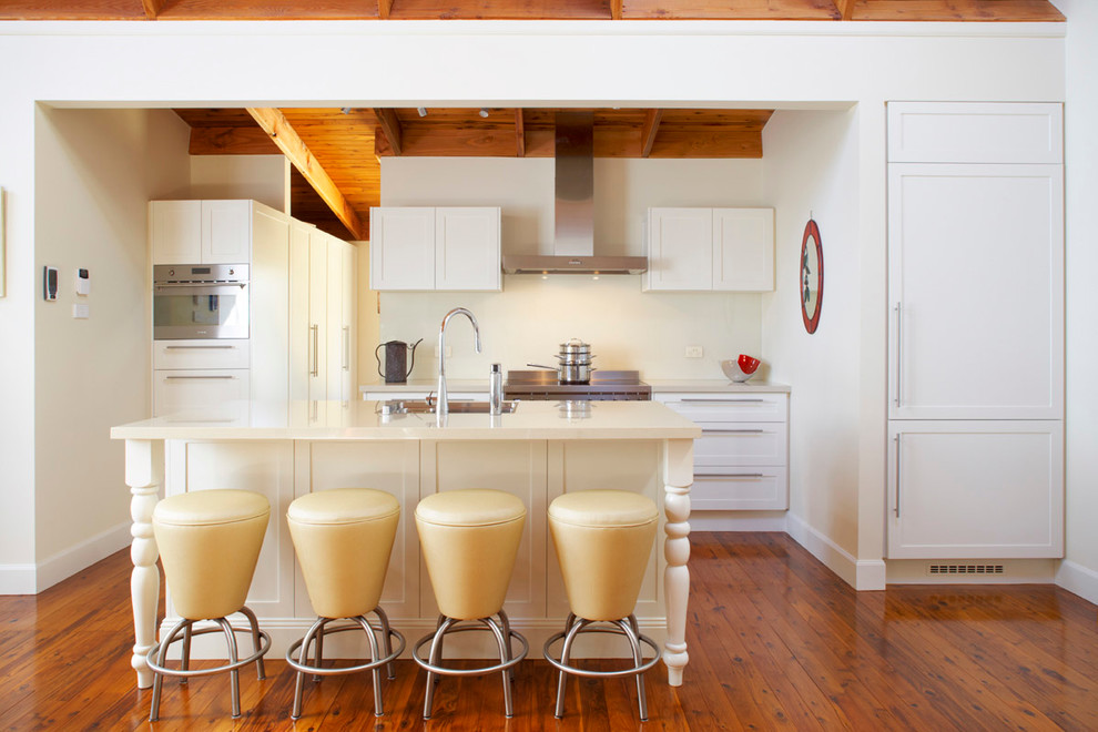 Klassische Küche mit Schrankfronten im Shaker-Stil, weißen Schränken, Küchenrückwand in Beige, Küchengeräten aus Edelstahl, braunem Holzboden und Kücheninsel in Sydney