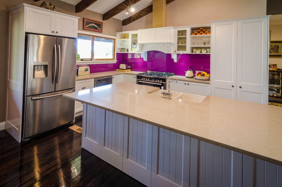Mid-sized elegant l-shaped dark wood floor eat-in kitchen photo in Sydney with a farmhouse sink, shaker cabinets, white cabinets, quartz countertops, pink backsplash, glass sheet backsplash, stainless steel appliances and an island