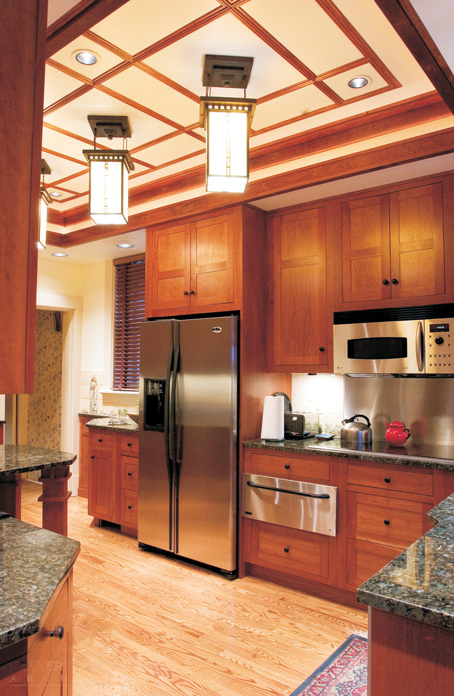 Photo of a small classic galley enclosed kitchen in Other with a submerged sink, shaker cabinets, medium wood cabinets, granite worktops, white splashback, ceramic splashback, stainless steel appliances, light hardwood flooring and a breakfast bar.