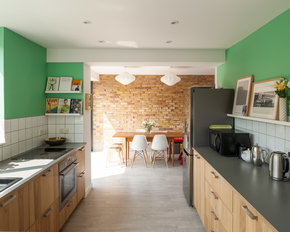 Large contemporary galley kitchen in London with a built-in sink, flat-panel cabinets, medium wood cabinets, composite countertops, white splashback, ceramic splashback, stainless steel appliances and light hardwood flooring.