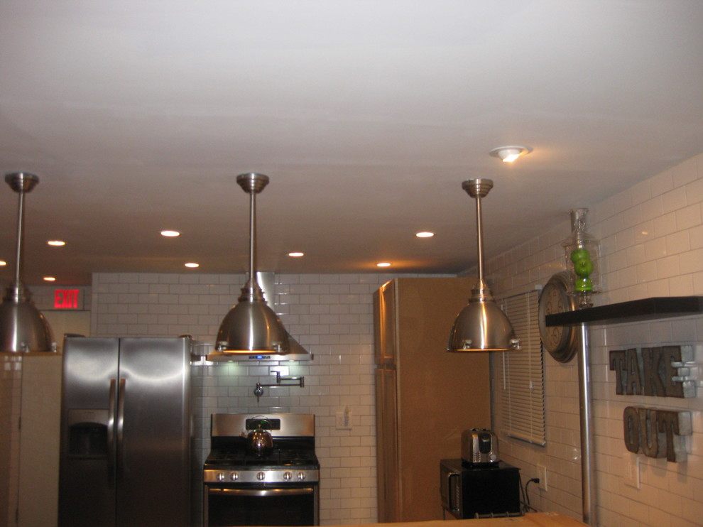 ニューヨークにある中くらいなインダストリアルスタイルのおしゃれなキッチン (シェーカースタイル扉のキャビネット、淡色木目調キャビネット、木材カウンター、白いキッチンパネル、サブウェイタイルのキッチンパネル、シルバーの調理設備、無垢フローリング、茶色い床) の写真