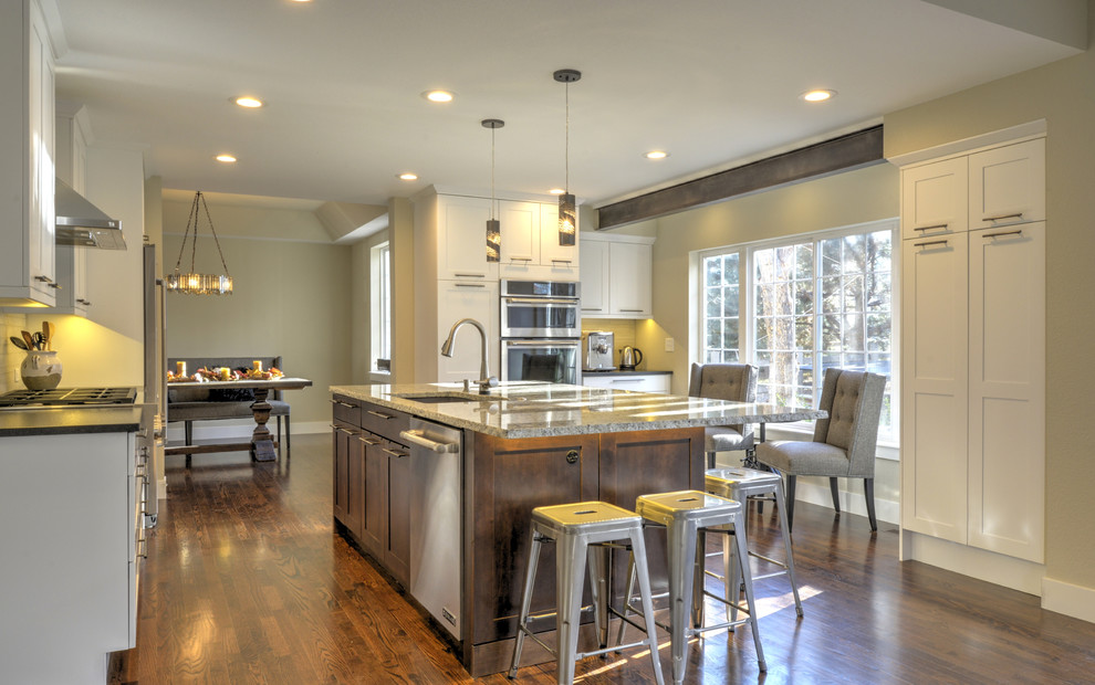 Large transitional u-shaped dark wood floor and brown floor enclosed kitchen photo in Denver with a single-bowl sink, shaker cabinets, white cabinets, granite countertops, ceramic backsplash, stainless steel appliances and an island