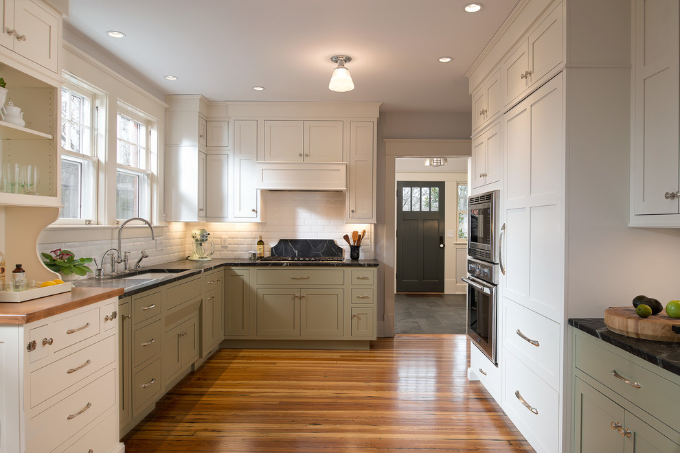 Inspiration for a mid-sized transitional u-shaped medium tone wood floor eat-in kitchen remodel in Other with an undermount sink, shaker cabinets, soapstone countertops, white backsplash, ceramic backsplash, paneled appliances, no island and white cabinets